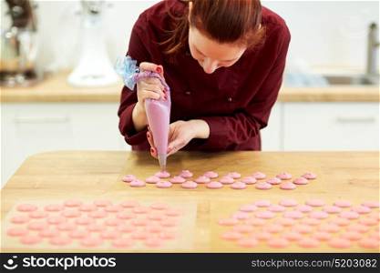 cooking, baking and people concept - chef with confectionery bag squeezing macaron batter or meringue cream to parchment paper at pastry shop kitchen. chef with injector squeezing macaron batter