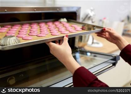 cooking, baking and people concept - chef with macarons on oven tray at bakery or confectionery. chef with macarons on oven tray at confectionery