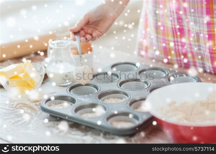 cooking, baking, food and home concept - close up of woman hand filling muffins molds with dough