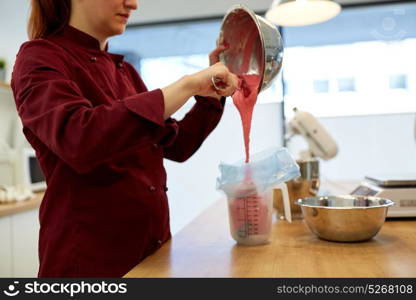 cooking, baking, food and people concept - chef pouring macaron batter or cream from bowl into measuring jug at pastry shop at kitchen. chef making macaron batter at kitchen