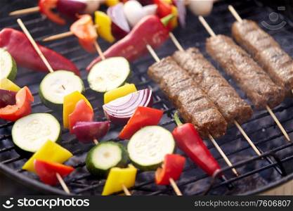 cooking, barbecue and food concept - close up of shish kebab meat and vegetables on bamboo skewers roasting to hot brazier grill outdoors. close up of barbecue kebab meat roasting on grill
