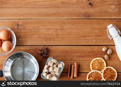 cooking, christmas and seasonal drinks concept - ingredients for eggnog, pot on wooden background. ingredients for eggnog, sugar and spices on wood