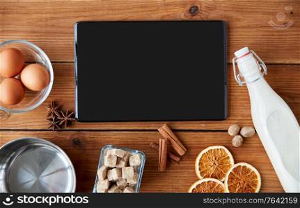 cooking, christmas and seasonal drinks concept - tablet pc computer, ingredients for eggnog, pot on wooden background. tablet pc, ingredients for eggnog cooking