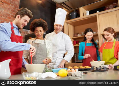 cooking class, culinary, bakery, food and people concept - happy group of friends and male chef cook baking in kitchen