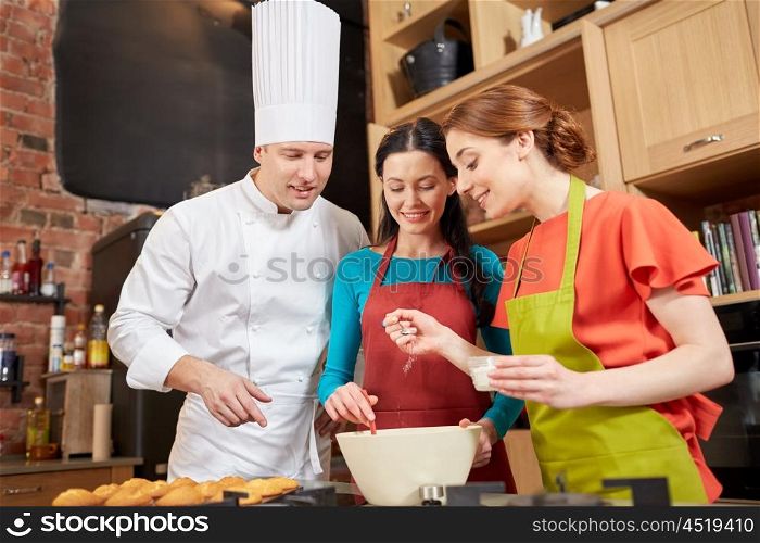cooking class, culinary, bakery, food and people concept - happy group of women and male chef cook baking muffins in kitchen