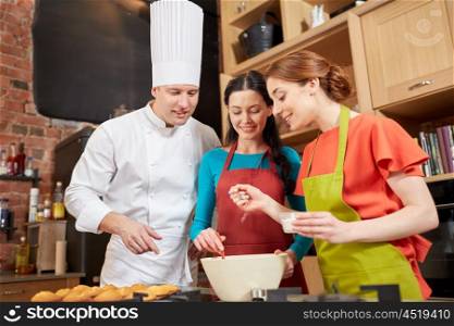 cooking class, culinary, bakery, food and people concept - happy group of women and male chef cook baking muffins in kitchen