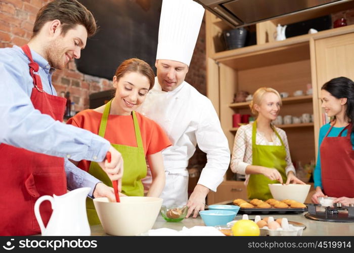 cooking class, culinary, bakery, food and people concept - happy group of friends and male chef cook baking in kitchen