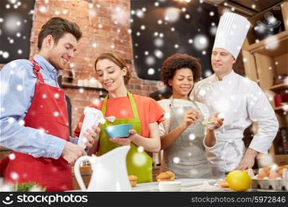 cooking class, culinary, bakery, food and people concept - happy group of friends and male chef cook baking in kitchen over snow effect