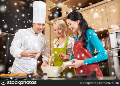 cooking class, culinary, bakery, food and people concept - happy group of women and male chef cook baking muffins in kitchen over snow effect