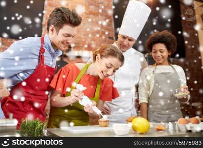 cooking class, culinary, bakery, food and people concept - happy group of friends and male chef cook baking in kitchen over snow effect