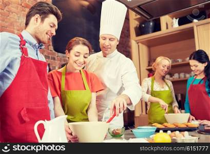 cooking class, culinary, bakery, food and people concept - happy group of friends and male chef cook baking in kitchen
