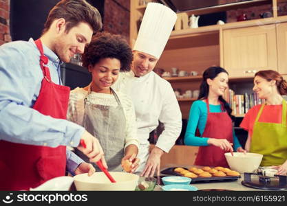 cooking class, culinary, bakery, food and people concept - happy group of friends and male chef cook baking in kitchen