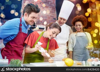 cooking class, culinary, bakery, food and people concept - happy group of friends and male chef cook baking in kitchen. happy friends and chef cook baking in kitchen