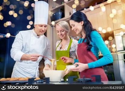 cooking class, culinary, bakery, food and people concept - happy group of women and male chef cook baking muffins in kitchen. happy women and chef cook baking in kitchen