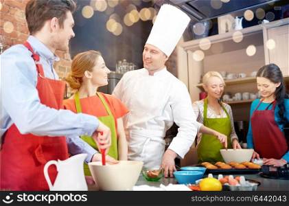 cooking class, culinary, bakery, food and people concept - happy group of friends and male chef cook baking in kitchen. happy friends and chef cook baking in kitchen