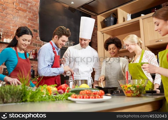 cooking class, culinary, food and people concept - happy group of friends and male chef cook cooking in kitchen