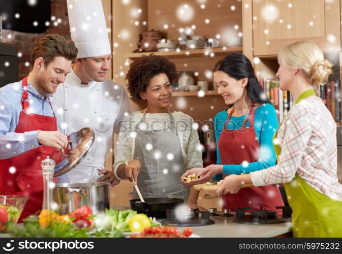 cooking class, culinary, food and people concept - happy group of friends and male chef cook cooking in kitchen over snow effect