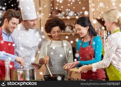 cooking class, culinary, food and people concept - happy group of friends and male chef cook cooking in kitchen over snow effect