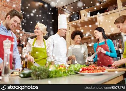 cooking class, culinary, food and people concept - happy group of friends with male chef cook cooking and talking in kitchen over snow effect