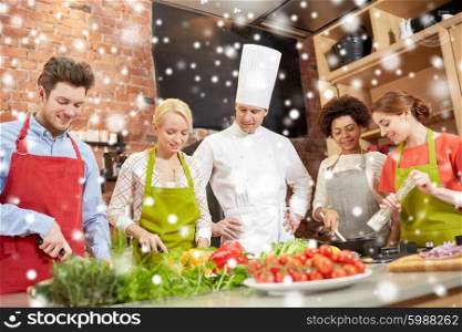 cooking class, culinary, food and people concept - happy group of friends with male chef cook cooking in kitchen over snow effect