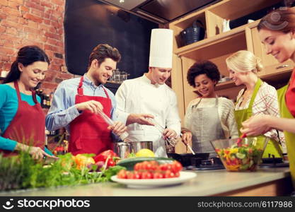 cooking class, culinary, food and people concept - happy group of friends and male chef cook cooking in kitchen