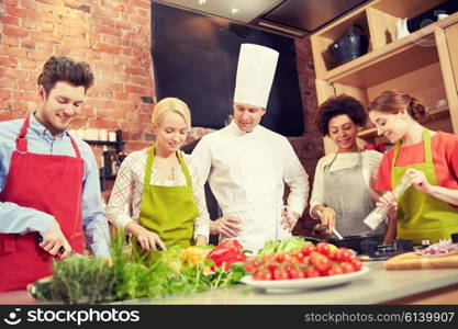 cooking class, culinary, food and people concept - happy group of friends with male chef cook cooking in kitchen