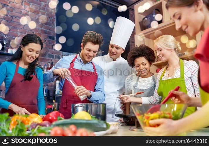 cooking class, culinary, food and people concept - happy group of friends and male chef cook cooking in kitchen. happy friends and chef cook cooking in kitchen