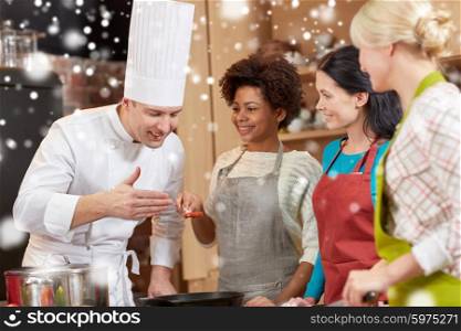 cooking class, culinary, food and people concept - happy group of women and male chef cook cooking in kitchen over snow effect