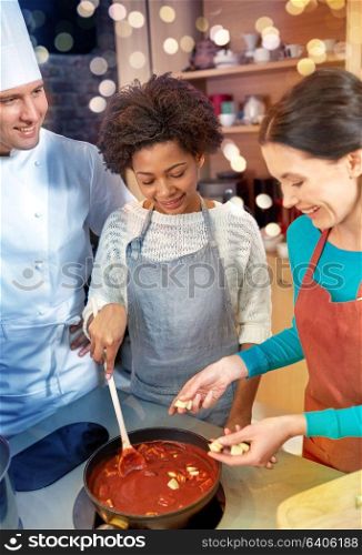 cooking class, culinary, food and people concept - happy group of women and male chef cook cooking tomato souse in kitchen. happy women and chef cook cooking in kitchen