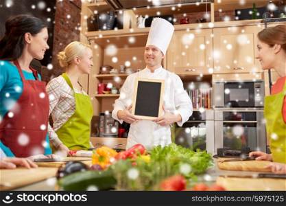 cooking class, culinary, food and people concept - happy women and chef cook with blank menu chalk board in kitchen over snow effect