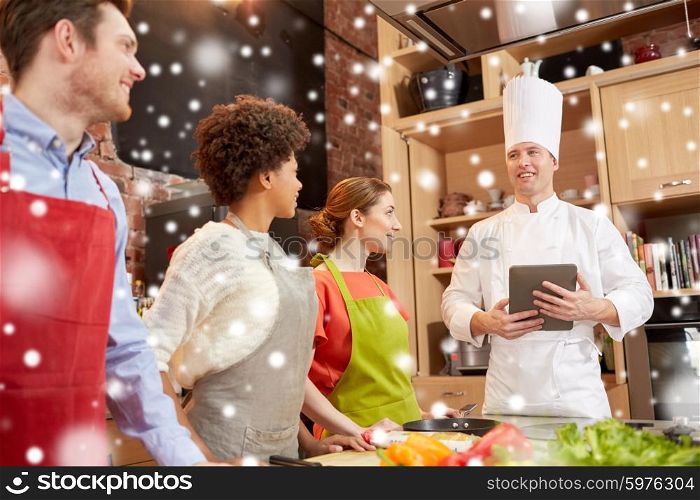 cooking class, culinary, food, technology and people concept - happy friends with tablet pc in kitchen over snow effect