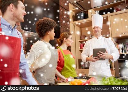 cooking class, culinary, food, technology and people concept - happy friends with tablet pc in kitchen over snow effect