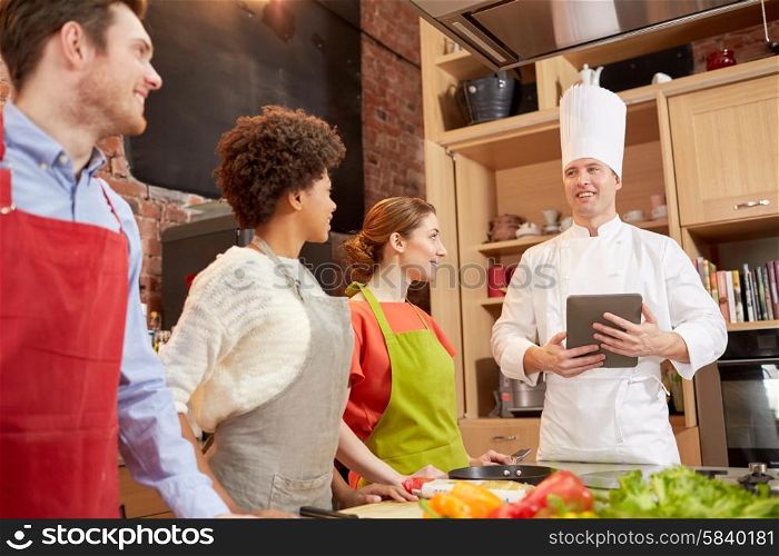 cooking class, culinary, food, technology and people concept - happy friends with tablet pc in kitchen