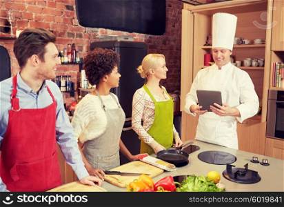 cooking class, culinary, food, technology and people concept - happy friends with tablet pc in kitchen