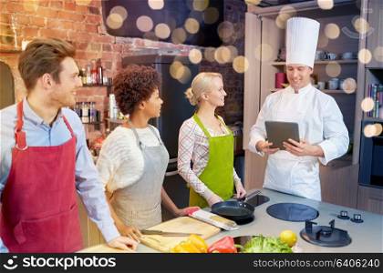 cooking class, culinary, food, technology and people concept - happy friends with tablet pc in kitchen. happy friends with tablet pc in kitchen