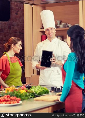 cooking class, culinary, food, technology and people concept - happy women with chef cook showing blank tablet pc screen in kitchen