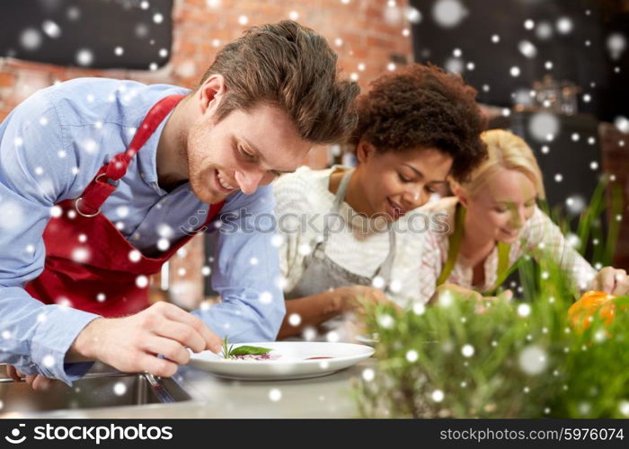 cooking class, friendship, food and people concept - happy women cooking and decorating plates with dishes in kitchen over snow effect