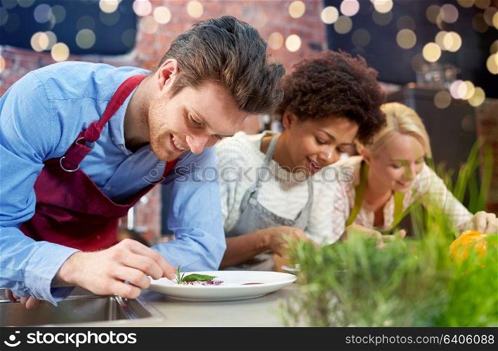 cooking class, friendship, food and people concept - happy women cooking and decorating plates with dishes in kitchen. happy friends cooking and decorating dishes
