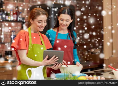 cooking class, friendship, food, technology and people concept - happy women with tablet pc computer in kitchen over snow effect