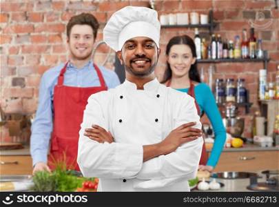 cooking class, profession and people concept - happy male indian chef in toque over students background. happy male indian chef in toque at cooking class