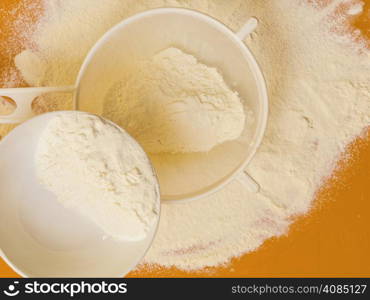 Cooking concept. Preparation for baking, bake ingredients and kitchen tools to make a cake, sifting wheat flour on orange nonstick silicone mat, top view