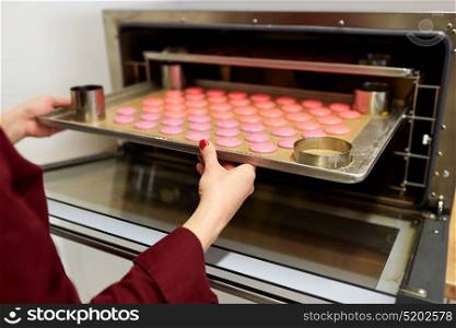 cooking, confectionery and people concept - chef with macarons on oven tray at bakery. chef with macarons on oven tray at confectionery