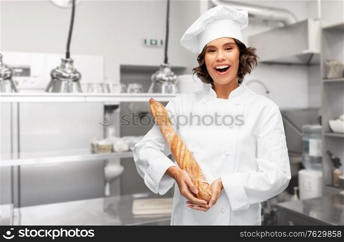 cooking, culinary and bakery concept - happy smiling female chef or baker in toque holding french bread or baguette over restaurant kitchen background. happy female chef with french bread or baguette
