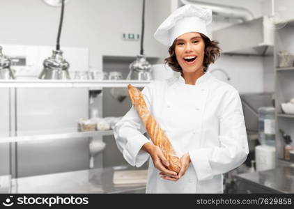 cooking, culinary and bakery concept - happy smiling female chef or baker in toque holding french bread or baguette over restaurant kitchen background. happy female chef with french bread or baguette