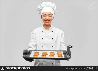 cooking, culinary and bakery concept - happy smiling female chef or baker in toque holding baking tray with oatmeal cookies over grey background. happy female chef with cookies on oven tray