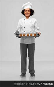 cooking, culinary and bakery concept - happy smiling female chef or baker in white toque and jacket holding baking tray with oatmeal cookies over grey background. happy female chef with cookies on oven tray