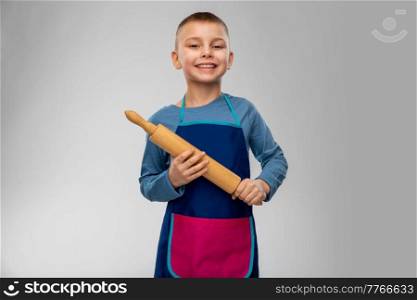 cooking, culinary and baking concept - happy smiling little boy in apron with rolling pin over grey background. smiling little boy in apron with rolling pin