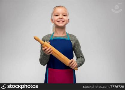 cooking, culinary and baking concept - happy smiling little girl in apron with rolling pin over grey background. smiling little girl in apron with rolling pin