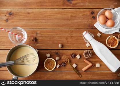 cooking, culinary and christmas drinks concept - pot with eggnog, ingredients and aromatic spices on wooden background. pot with eggnog, ingredients and spices on wood