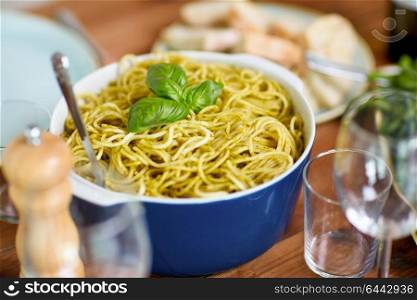 cooking, culinary and eating concept - pasta with basil in bowl and other food on wooden table. pasta with basil in bowl and other food on table